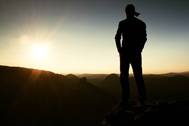 istock Hiker in cap on rock empire and watch to Sun. 493714072