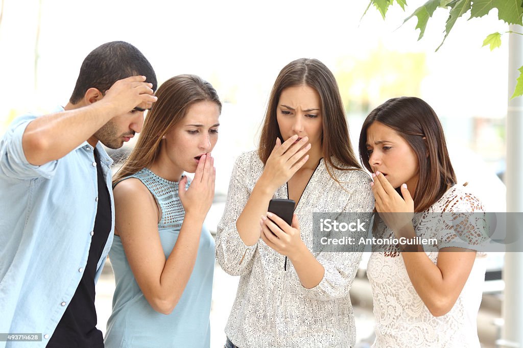 Four worried friends watching smart phone Four worried multi ethnic friends watching a smart phone in the street Social Media Stock Photo