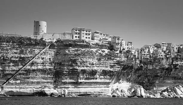 Old tower and houses on rocky coast in Bonifacio, Corsica island, France. Monochrome photo