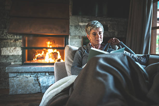 femme lisant un livre sur le divan - blanket fireplace winter women photos et images de collection