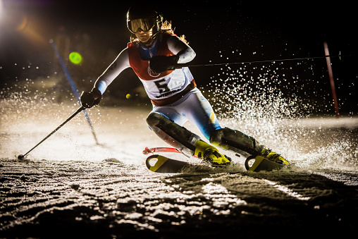 Professional alpine skier practicing slalom in the night, taking a sharp carving turn. Shadows, artificial lighting.