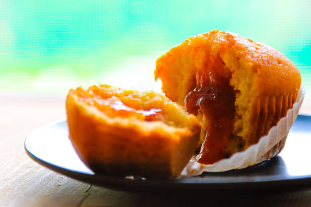 Open muffin with filling on black plate in a warmly lit breakfast scene. Marmalade filling is leaking from the inside of muffin.