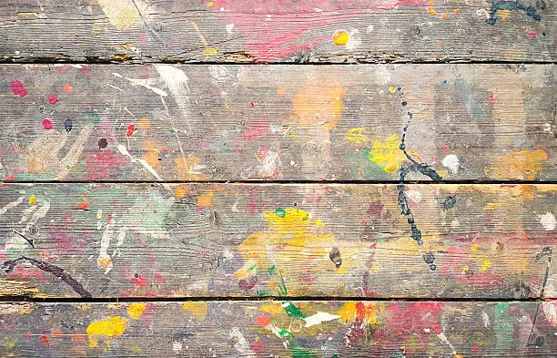 Photo of Multicoloured paint splatters on weathered wooden floorboards.