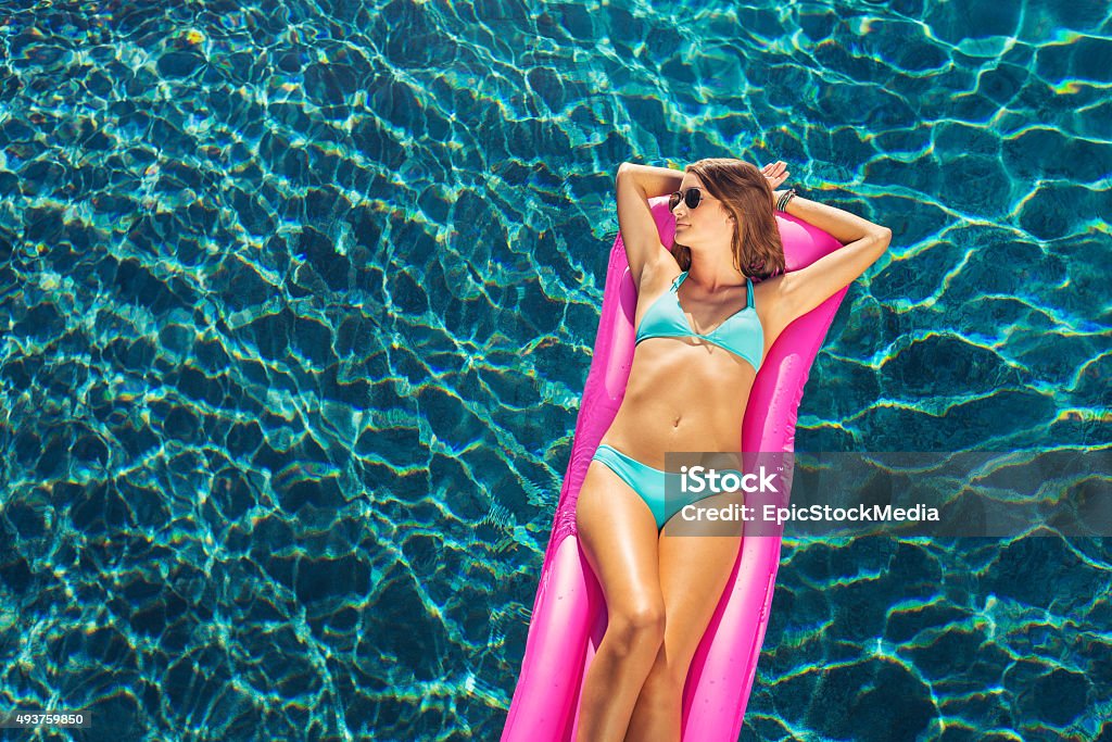 Beautiful Woman Relaxing Floating on Raft in Pool Beautiful sexy young woman in bikini relaxing floating on raft in luxury swimming pool 2015 Stock Photo