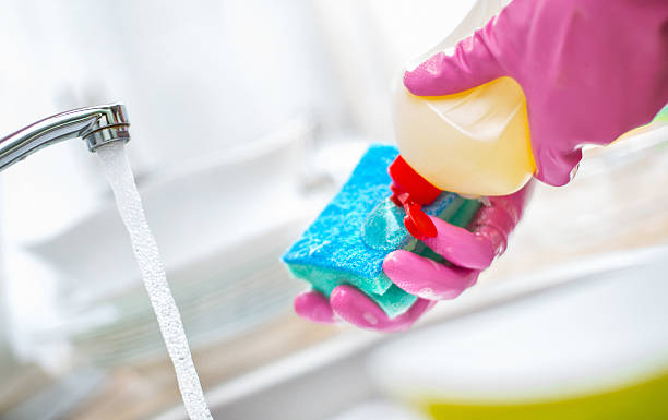 Dishwashing routine. Closeup of unrecognizable person applying dishwashing liquid onto cleaning sponge. The person is wearing pink protective gloves There's kitchen tap and blurry dishes in background.Tilt shot. serving dish stock pictures, royalty-free photos & images