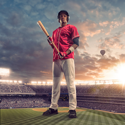 A conceptual image of a giant male baseball batter holding baseball bat with both hands and looking into the distance, standing in a generic baseball stadium full of spectators. The huge man is wearing red and white baseball kit, and towers above the floodlit ground under a dusky evening sky.