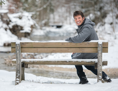 Happy handsome man enjoying this wonderful winter day on a bench in the snow.