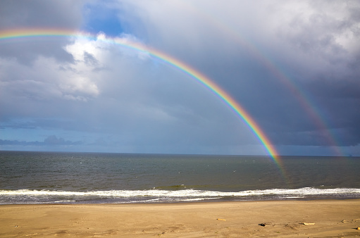 Rainbow over sea, cloudy sky, bech sand