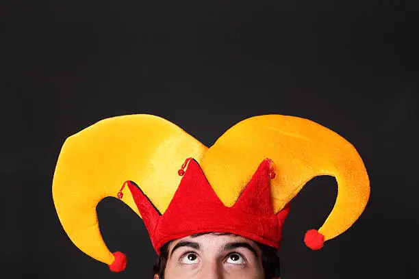 Young man wearing a jester's hat is looking upwards into blank space