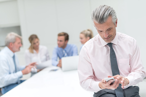 Senior man using his phone in a business meeting texting or using app - communications concepts