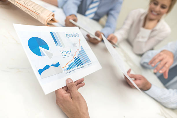 People in a business meeting checking the market behaviour Group of people in a business meeting checking the market behaviour and holding a document with statistics and bar graph photos stock pictures, royalty-free photos & images