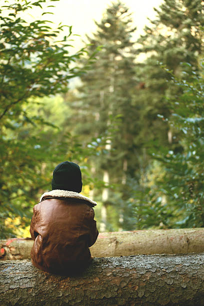istock Boy sitting on tree trunk looking into the distance 493787152