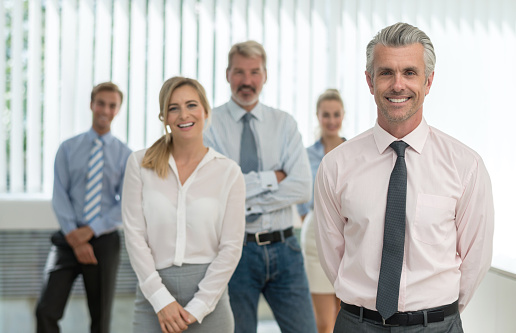 Happy Businessman Standing In Front Of His Colleagues In Office