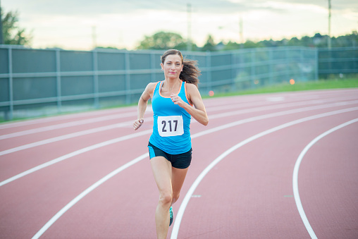 A woman is running in athletic clothing on a track during a race.