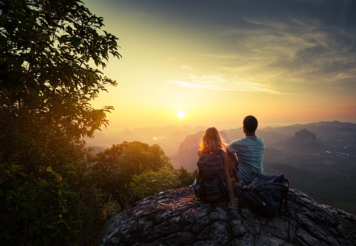 Two hikers on top of the mountain enjoying sunrise over the tropical valley