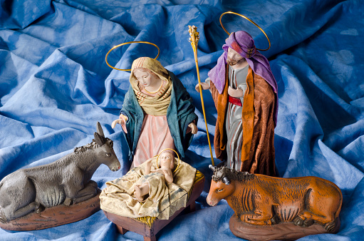 Christmas Crib. Figures of Baby Jesus, Virgin Mary and St. Joseph. Selective focus. Blue background.