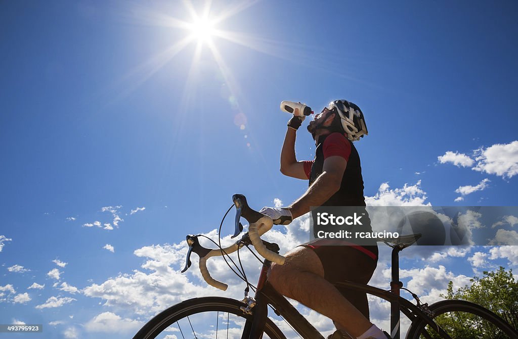 Cyclist resting and drinking isotonic drink. Cyclist resting and drinking isotonic drink. Backlight, sunny summer day. Cycling Stock Photo