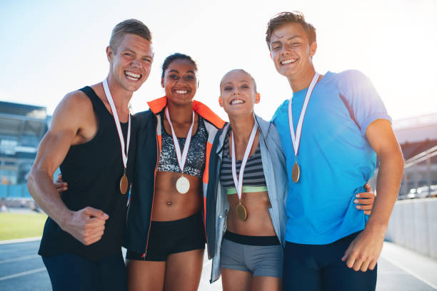 Happy multiracial athletes celebrating victory Happy multiracial athletes celebrating victory while standing together on racetrack. Group of runner with medals winning a competition. cheering group of people success looking at camera stock pictures, royalty-free photos & images