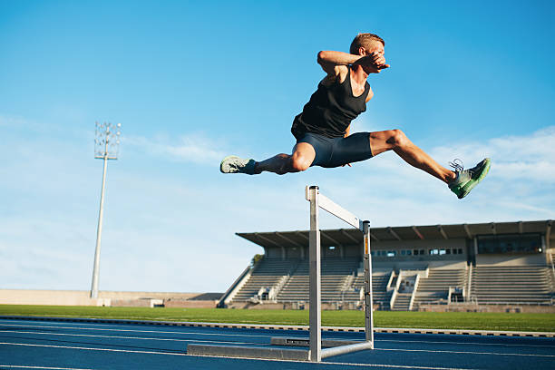 Professional sprinter jumping over a hurdle Professional male track and field athlete during obstacle race. Young athlete jumping over a hurdle during training on racetrack in athletics stadium. hurdle stock pictures, royalty-free photos & images
