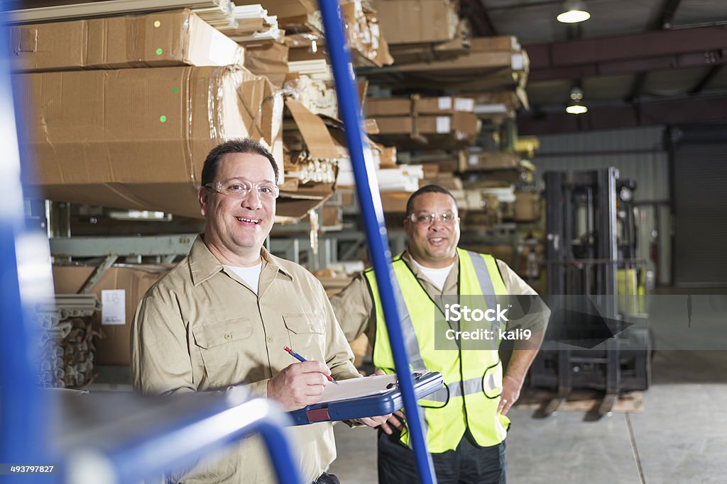 Workers in warehouse Multi-ethnic mature men working in warehouse.  Focus on man on left (40s) holding clipboard. 40-44 Years Stock Photo