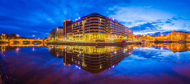 Deep blue dusk skies above the illuminated hotels, shops and apartment buildings reflecting in the tranquil waters of Kaisaniemenlahti in the heart of Helsinki, Finland's vibrant capital city. ProPhoto RGB profile for maximum color fidelity and gamut.