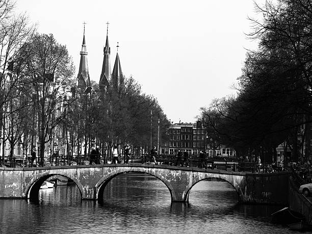 Gracht or Canal of Amsterdam with typical low bridge in early springtime, Netherlands. Black and white image.