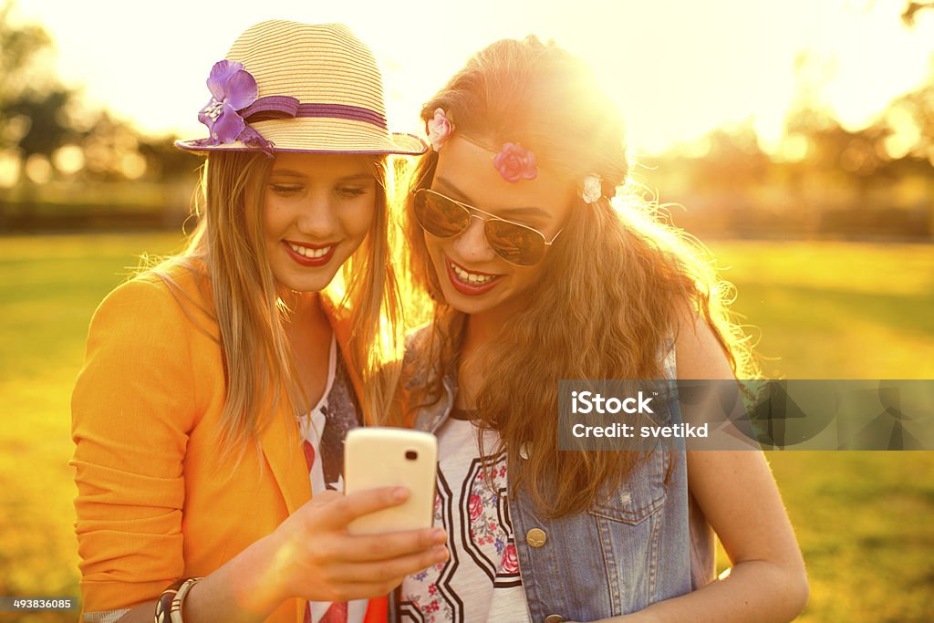 Young women enjoying outdoors. Young women enjoying outdoors in sunset, using smartphone. Adult Stock Photo