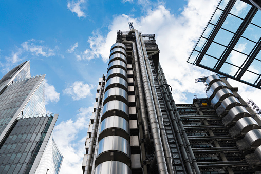 London, United Kingdom - March 23, 2014: Wide-angle view of the Lloyds Building and other skyscrapers in the City of London, UK. Designed by architect Richard Rogers and built between 1978 and 1986, the Lloyds Building is located on the former site of East India House in Lime Street. The building is a leading example of radical Bowellism architecture in which the services for the building, such as ducts and lifts, are located on the exterior to maximise space in the interior.