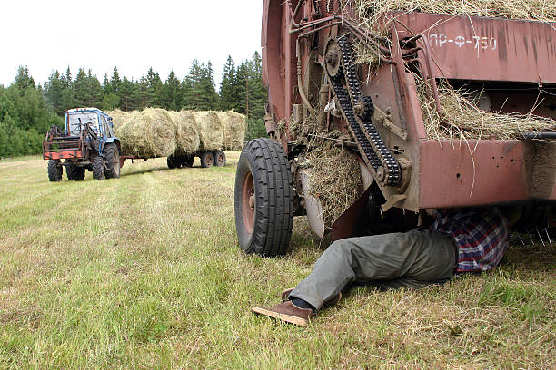 Farmer repairing round baler, in field, during hay. Lemozero, Olonets, Karelia, Russia - July 15, 2006: Farmer repairing tractor in field, during hay. hay baler stock pictures, royalty-free photos & images