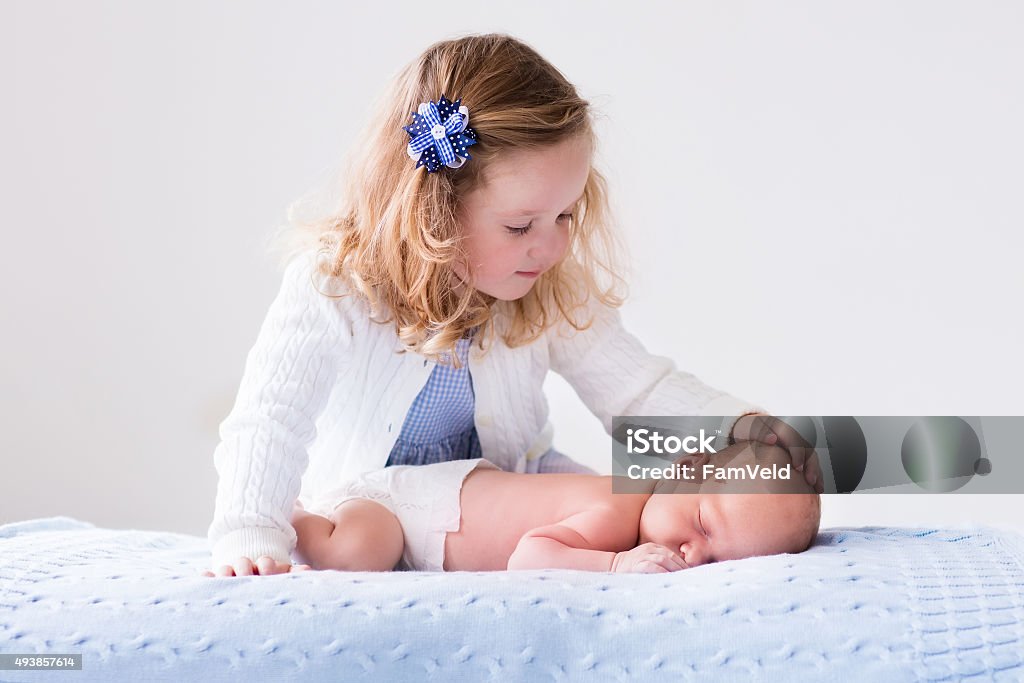 Little girl playing with newborn baby brother Little sister hugging her newborn brother. Toddler kid meeting new sibling. Cute girl and new born baby boy relax in a white bedroom. Family with children at home. Love, trust and tenderness concept. Sibling Stock Photo