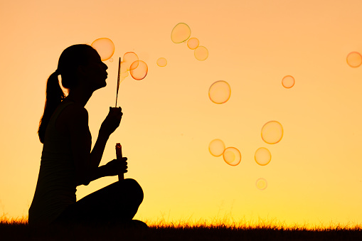 Silhouette of woman blowing bubbles.