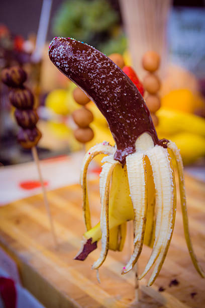 Banana on a stick coated chocolate with coconut chips and colored candies.Blur background.