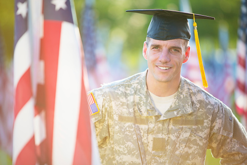 Portrait of American Soldier with graduation hat in front of American flags. 