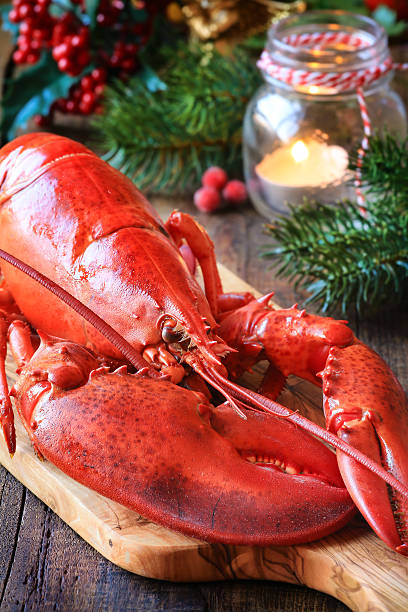 Christmas lobster Delicious cooked lobster on wooden cutting board as a concept of Christmas cooking with a candle and fir or pine branches at the  background lobster seafood photos stock pictures, royalty-free photos & images