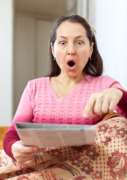 amazed mature woman looks newspaper fright and amazed mature woman looks newspaper at home wonderingly stock pictures, royalty-free photos & images