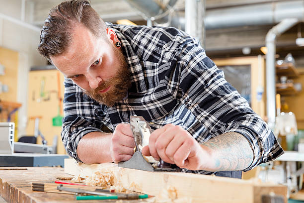 istock Focused carpenter work with plane on wood plank in workshop 493891136