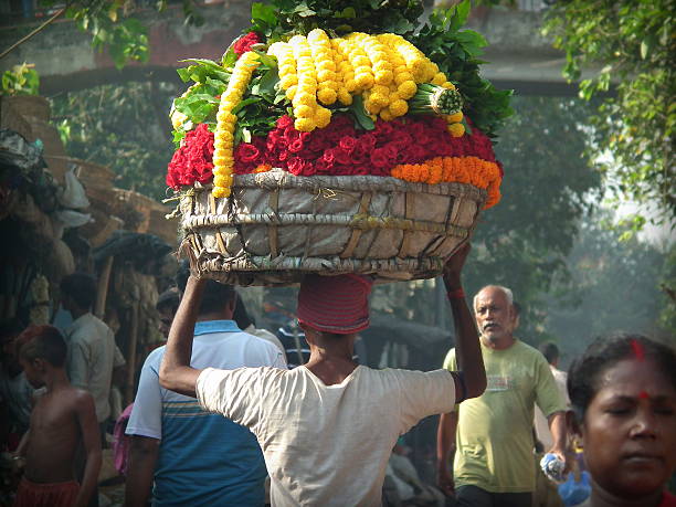 Man carrying flowers in a basket Kolkata, India - October 24, 2015: Unidentified man carrying flowers on a basket atop his head at the 'Barabajar Flower Market' at early morning nearby the Howrah Bridge, Kolkata. flower market stock pictures, royalty-free photos & images