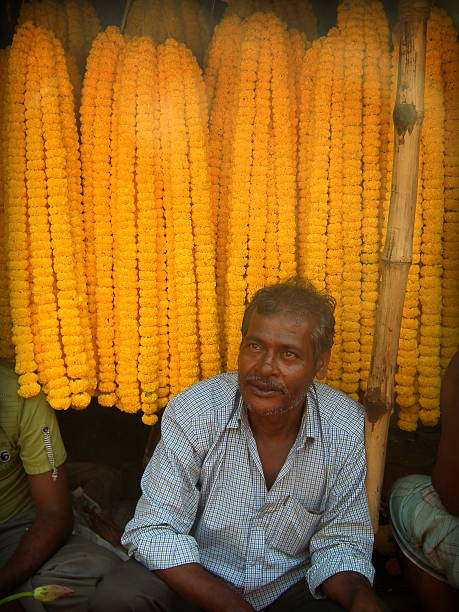 Man selling Garlands made of Marigold Kolkata, India - October 24, 2015: Unidentified Marigold (Genda) flower seller sitting infront his flowers at 'Barabajar Flower Market' at early morning nearby the Howrah Bridge, Kolkata. flower market morning flower selling stock pictures, royalty-free photos & images