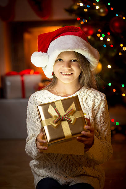 istock girl posing against fireplace and Christmas tree with gift box 493910246