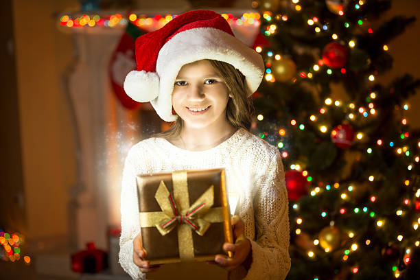 istock smiling girl posing with shining gift box against Christmas tree 493910288