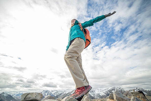 Young hiker woman standing on a rock at the mountain top arms outstretched for freedom and positive emotion.