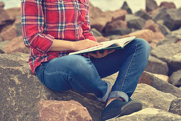 istock girl sitting on rock and reading a book 493917180