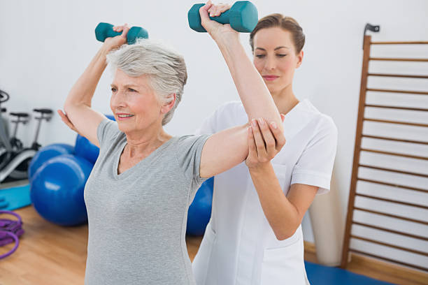 istock Trainer assisting senior woman lifting weights 493918401