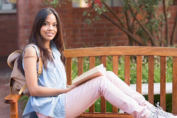 istock Female student with book sitting on bench 493918481