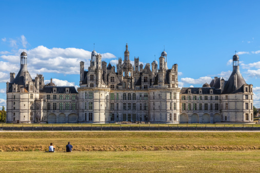 Chambord,France-September 08,2013: Unidentified couple siting on the grass and admiring the Chambord Castle. Chambord is royal medieval French castle in Loire Valley - UNESCO heritage site.