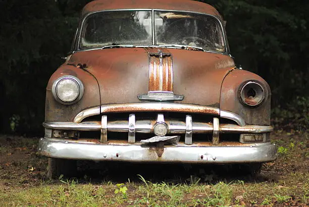 Rusty old Pontiac car melding into the ground beneath its sunken tires.