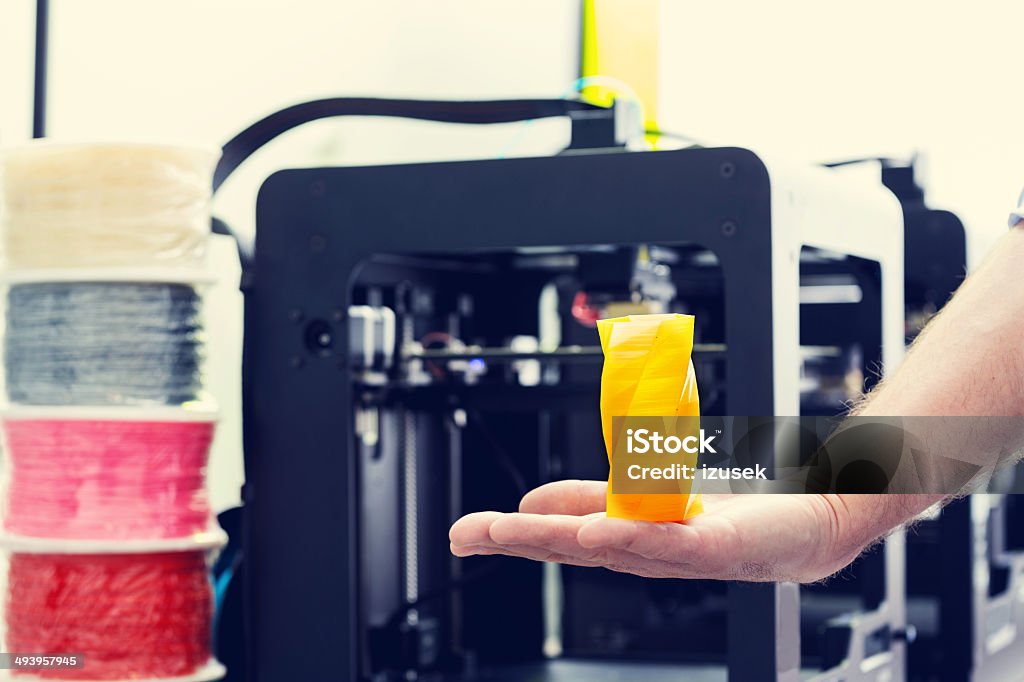 3D printer office Close up of yellow container printed by 3d printer on a human hand with 3d printer machines in the background. 3D Printing Stock Photo