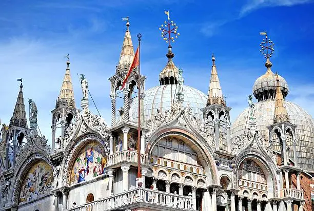 A bright blue but cloud dusted sky contrasts with the immensely ornately decorated domes, arches and spires of Basilica Cattedrale Patriarcale di San Marco.The most famous of the Venice's churches its one of the best known examples of Italo-Byzantine architecture