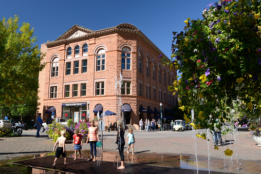 Aspen, USA - September 26, 2015. Tourists in downtown Aspen with children playing with fountain on Mill Street. Aspen is an upscale ski resort town nestled in Colorado's Rocky Mountains. It attracts tourists year-round for its variety of restaurants, art galleries and surrounding mountain scenery.