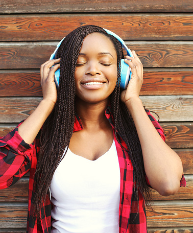 Beautiful smiling african woman with headphones enjoying listens to music in city